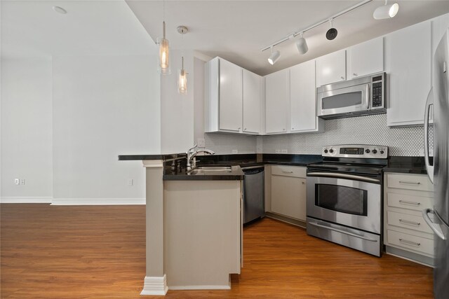 kitchen featuring appliances with stainless steel finishes, kitchen peninsula, hardwood / wood-style flooring, and track lighting