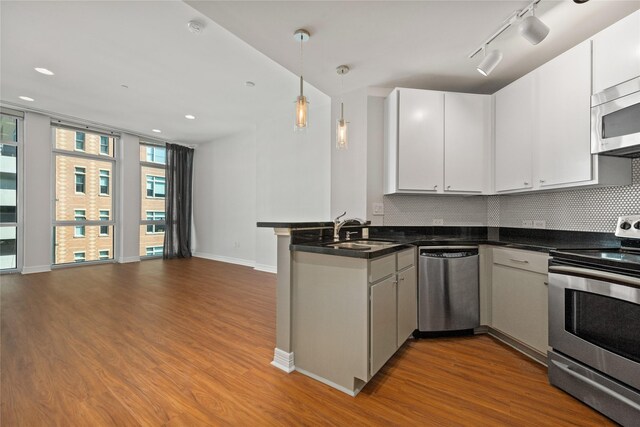 kitchen featuring appliances with stainless steel finishes, kitchen peninsula, decorative backsplash, rail lighting, and wood-type flooring