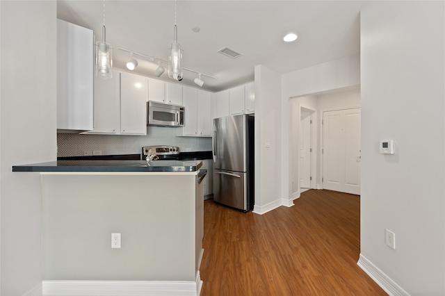 kitchen with hardwood / wood-style flooring, stainless steel appliances, rail lighting, white cabinets, and decorative backsplash