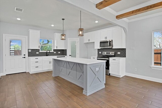 kitchen featuring beam ceiling, appliances with stainless steel finishes, a kitchen island, and plenty of natural light