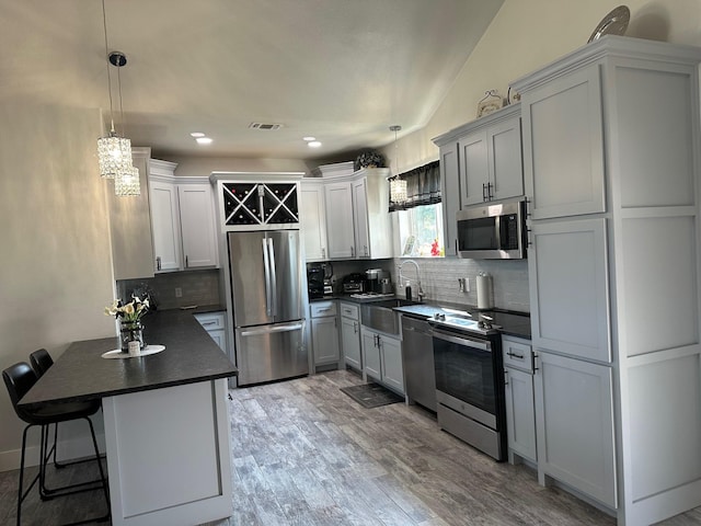 kitchen with a kitchen breakfast bar, light wood-type flooring, stainless steel appliances, sink, and hanging light fixtures