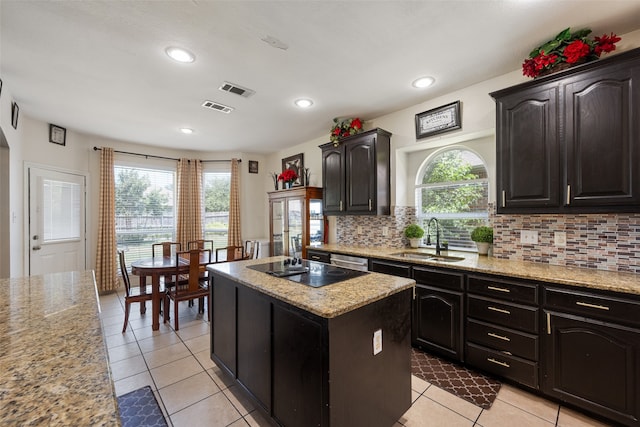 kitchen with sink, light stone counters, backsplash, and a center island