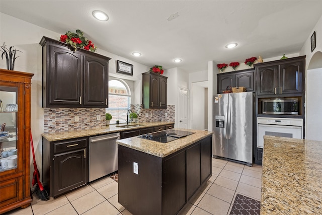 kitchen with decorative backsplash, appliances with stainless steel finishes, light stone countertops, light tile patterned flooring, and a kitchen island