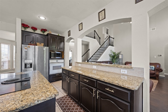 kitchen with appliances with stainless steel finishes, dark brown cabinets, light stone countertops, hardwood / wood-style floors, and a kitchen island