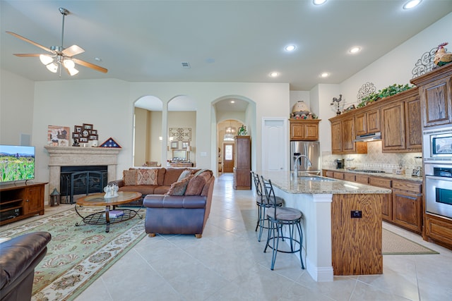 kitchen featuring light tile patterned floors, decorative backsplash, appliances with stainless steel finishes, an island with sink, and ceiling fan