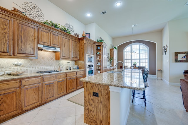 kitchen with light tile patterned floors, appliances with stainless steel finishes, a center island with sink, sink, and tasteful backsplash