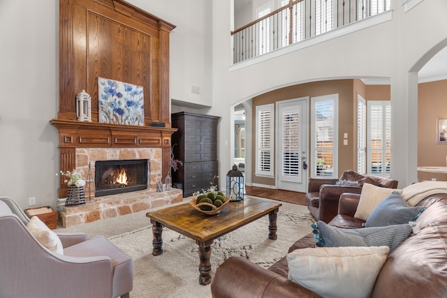 living room with hardwood / wood-style floors, a towering ceiling, a stone fireplace, and ornamental molding