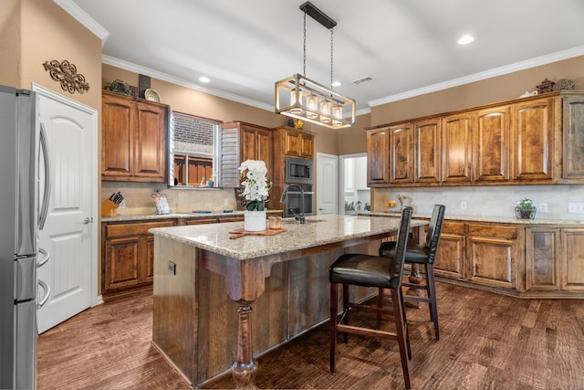 kitchen featuring a kitchen island with sink, dark hardwood / wood-style floors, ornamental molding, appliances with stainless steel finishes, and decorative light fixtures