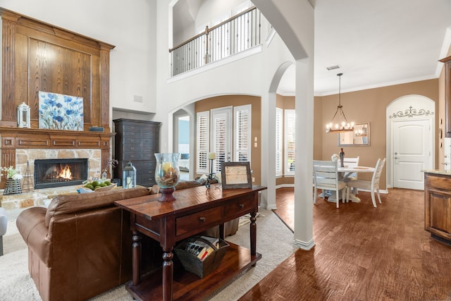 living room featuring ornamental molding, a towering ceiling, a chandelier, a fireplace, and hardwood / wood-style flooring