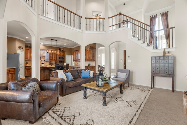 carpeted living room with ceiling fan with notable chandelier, a high ceiling, and ornamental molding