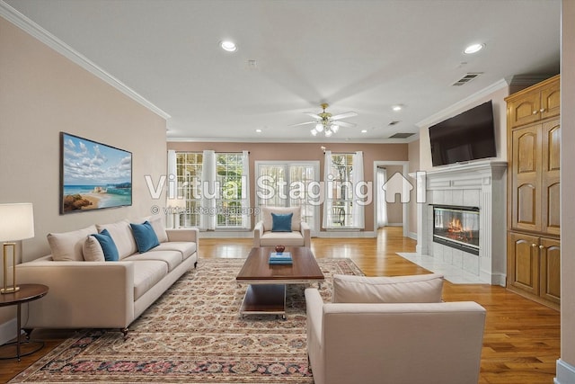 living room featuring ceiling fan, crown molding, a fireplace, and wood-type flooring