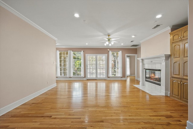 unfurnished living room with crown molding, ceiling fan, a tiled fireplace, and light wood-type flooring