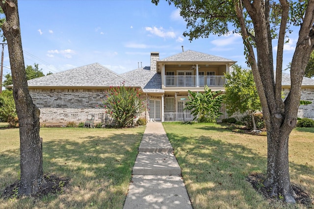 view of front of property with ceiling fan, a balcony, and a front lawn