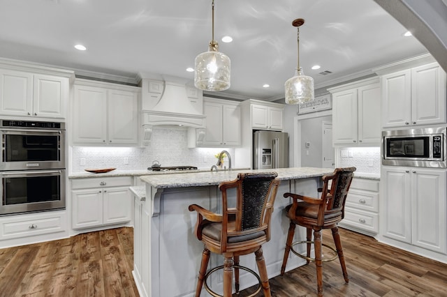 kitchen featuring white cabinets, custom exhaust hood, stainless steel appliances, and an island with sink