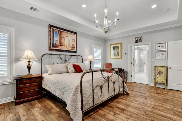 bedroom featuring a raised ceiling, crown molding, hardwood / wood-style flooring, connected bathroom, and a chandelier