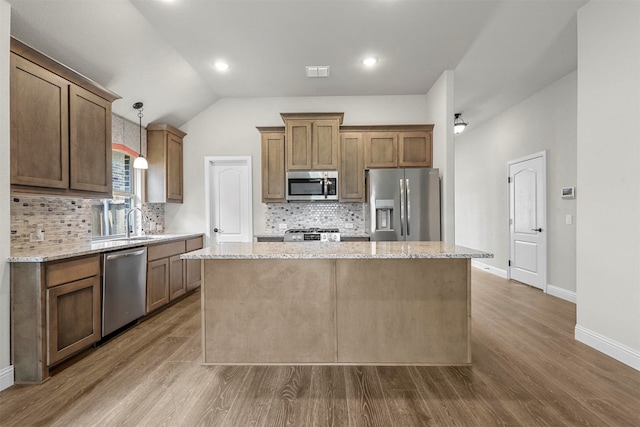 kitchen with pendant lighting, a center island, vaulted ceiling, appliances with stainless steel finishes, and light stone counters