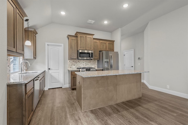 kitchen with light stone countertops, appliances with stainless steel finishes, a center island, and sink