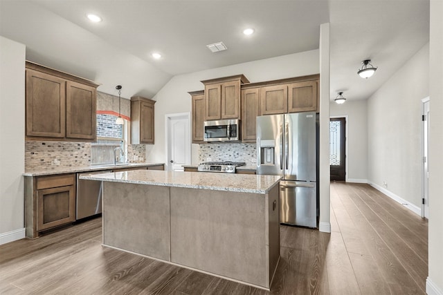 kitchen with appliances with stainless steel finishes, light stone counters, vaulted ceiling, pendant lighting, and a kitchen island