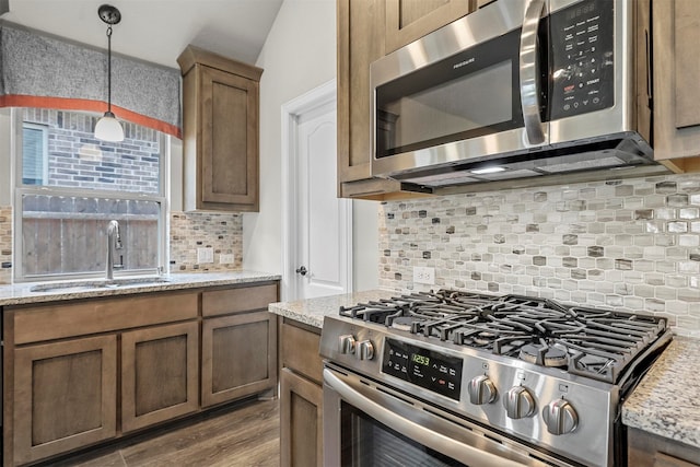 kitchen featuring light stone countertops, sink, stainless steel appliances, decorative light fixtures, and decorative backsplash