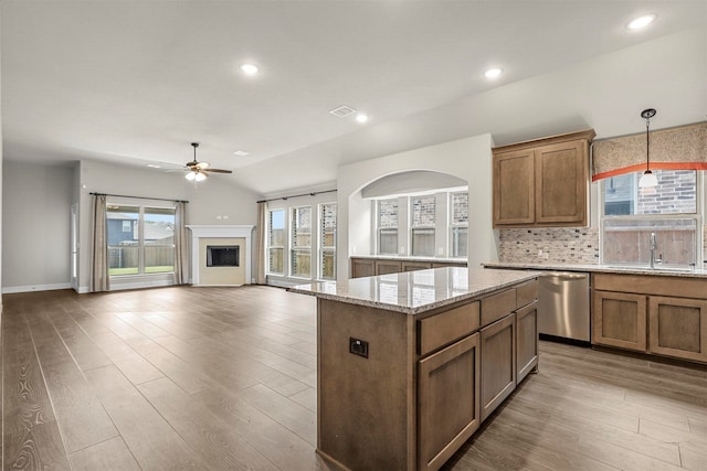 kitchen featuring light stone countertops, sink, hanging light fixtures, stainless steel dishwasher, and a kitchen island