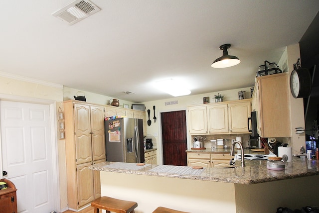 kitchen featuring kitchen peninsula, ornamental molding, sink, stainless steel fridge with ice dispenser, and a kitchen bar