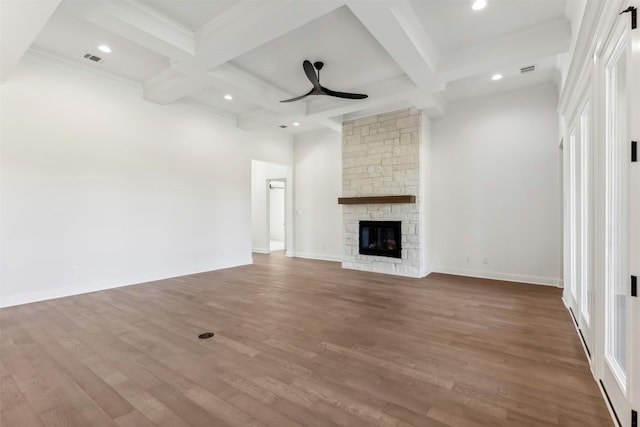 unfurnished living room featuring ceiling fan, beam ceiling, a stone fireplace, and wood-type flooring