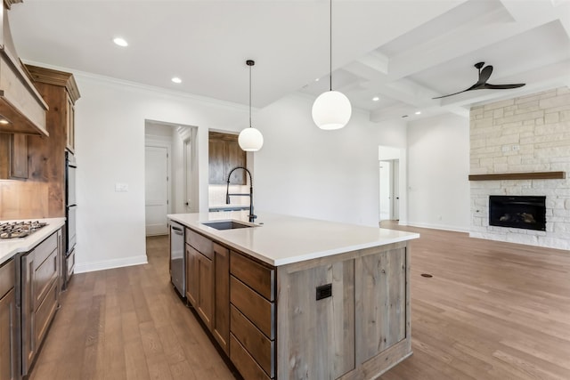 kitchen featuring pendant lighting, coffered ceiling, sink, ceiling fan, and an island with sink