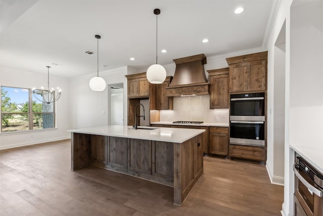 kitchen featuring appliances with stainless steel finishes, premium range hood, sink, decorative light fixtures, and an inviting chandelier