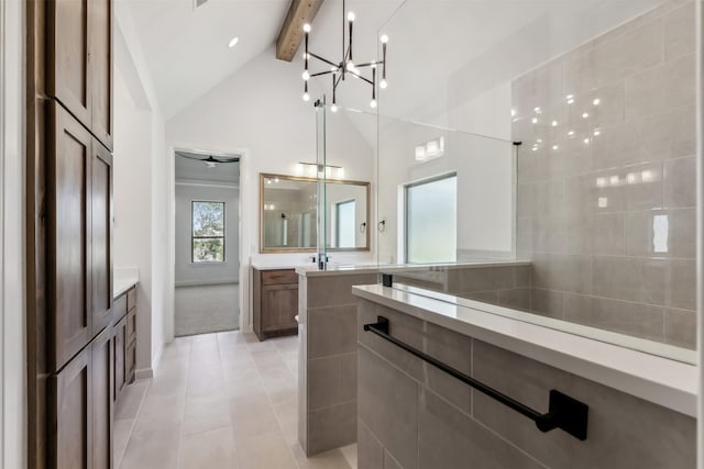 bathroom featuring vanity, a shower, ceiling fan with notable chandelier, tile patterned flooring, and vaulted ceiling with beams