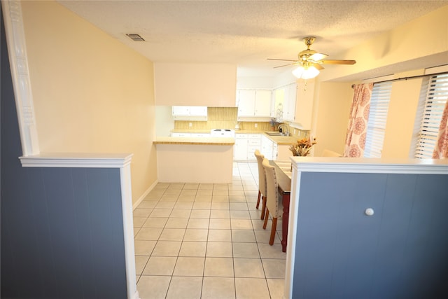 kitchen featuring sink, tasteful backsplash, light tile patterned floors, kitchen peninsula, and white cabinets