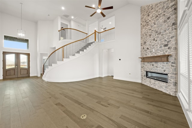 unfurnished living room featuring hardwood / wood-style floors, a stone fireplace, high vaulted ceiling, and ceiling fan with notable chandelier