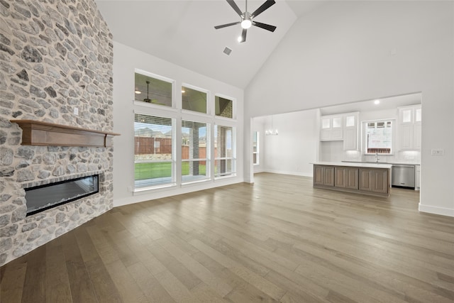 unfurnished living room featuring light hardwood / wood-style flooring, ceiling fan, a wealth of natural light, and a stone fireplace