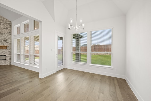 unfurnished dining area with light wood-type flooring, high vaulted ceiling, a chandelier, and a stone fireplace