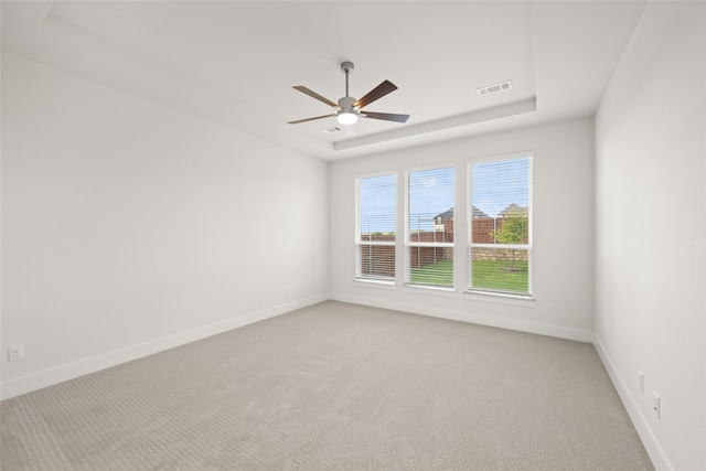 carpeted spare room with a raised ceiling and ceiling fan