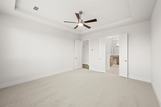 unfurnished bedroom featuring light carpet, a raised ceiling, ensuite bathroom, and ceiling fan