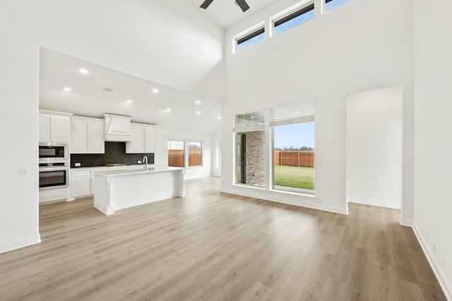 kitchen featuring built in microwave, premium range hood, oven, a kitchen island with sink, and white cabinets