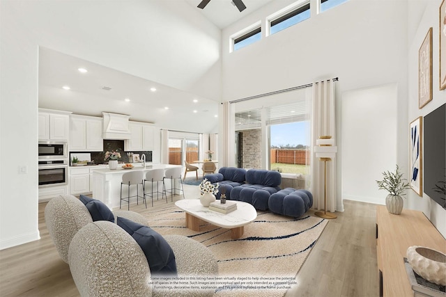 living room featuring ceiling fan, light hardwood / wood-style flooring, a healthy amount of sunlight, and a high ceiling