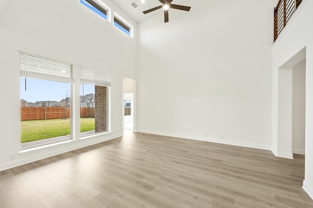 unfurnished living room featuring a towering ceiling, light hardwood / wood-style flooring, and ceiling fan