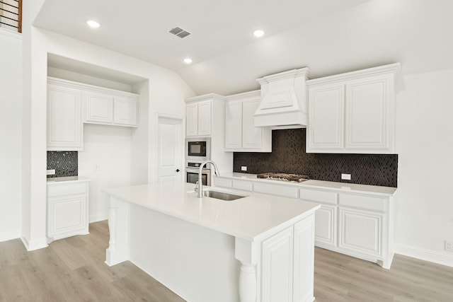 kitchen with premium range hood, white cabinetry, sink, stainless steel appliances, and a center island with sink