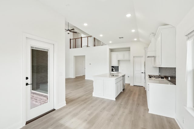 kitchen featuring white cabinetry, tasteful backsplash, high vaulted ceiling, light hardwood / wood-style floors, and a kitchen island with sink