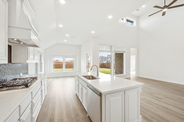 kitchen with a kitchen island with sink, white cabinets, sink, appliances with stainless steel finishes, and custom range hood