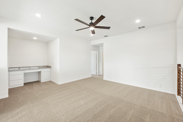 empty room with light carpet, ceiling fan, and built in desk