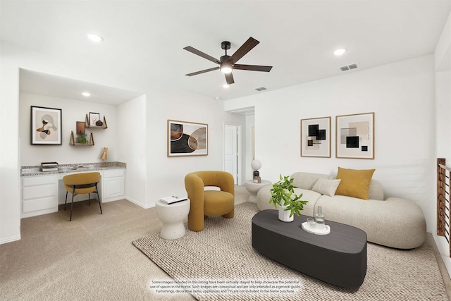 carpeted living room featuring ceiling fan and built in desk