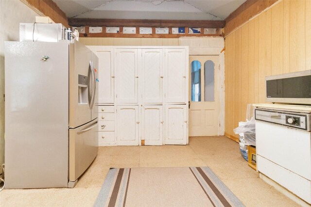 kitchen with wood walls, white cabinetry, and white fridge with ice dispenser