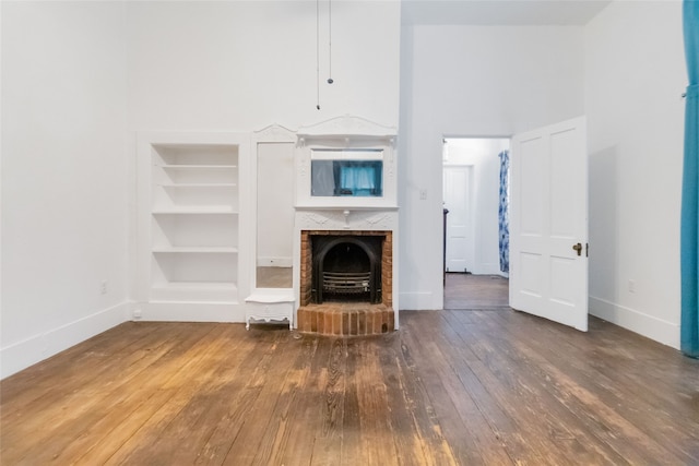 unfurnished living room featuring wood-type flooring, a fireplace, and built in shelves