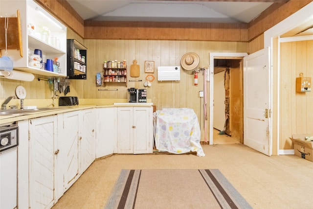 kitchen with light carpet, wooden walls, white dishwasher, and white cabinetry