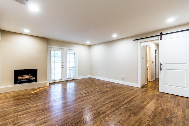 unfurnished living room with dark hardwood / wood-style floors, a barn door, and french doors