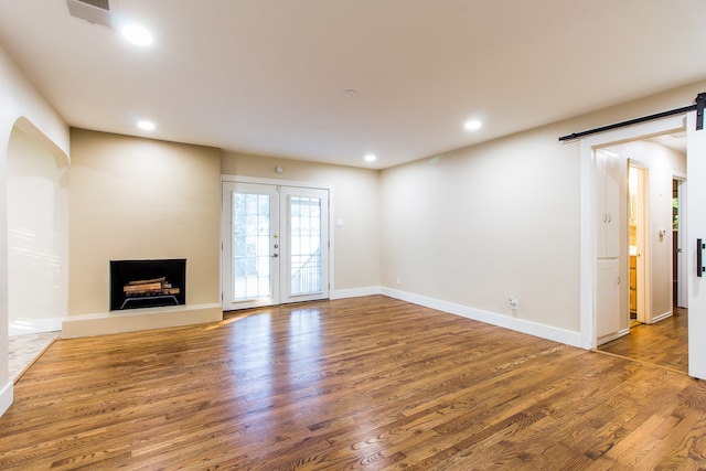 unfurnished living room with a barn door, hardwood / wood-style flooring, and french doors