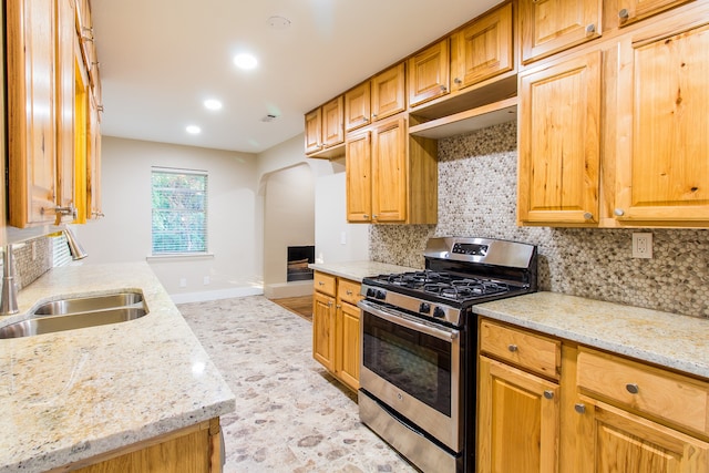 kitchen featuring sink, stainless steel range with gas stovetop, backsplash, and light stone counters