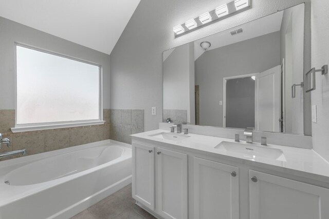 bathroom featuring double sink vanity, tile patterned floors, vaulted ceiling, and a bathtub